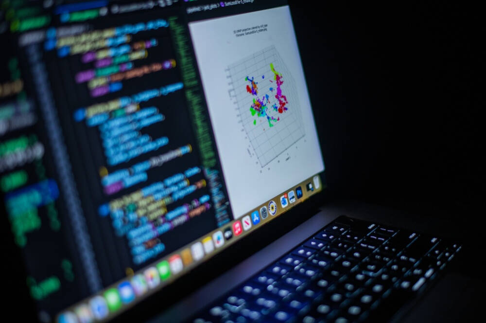 A laptop screen displaying colorful programming code on the left and a 3D scatter plot with multicolored data points on the right, set against a dark background.